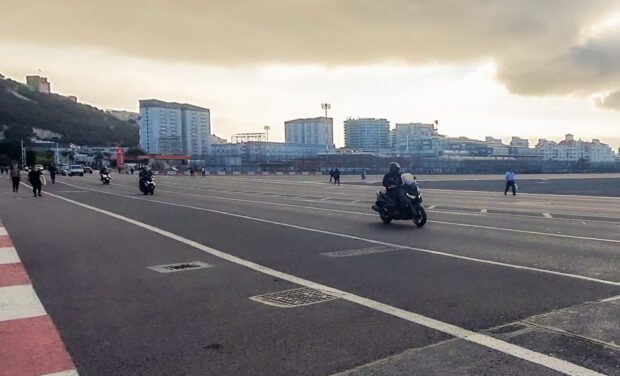 A man rides a motorcycle along a road which bisects a runway