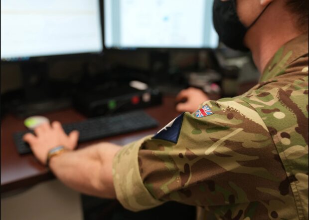 A man in military clothing sits at a computer