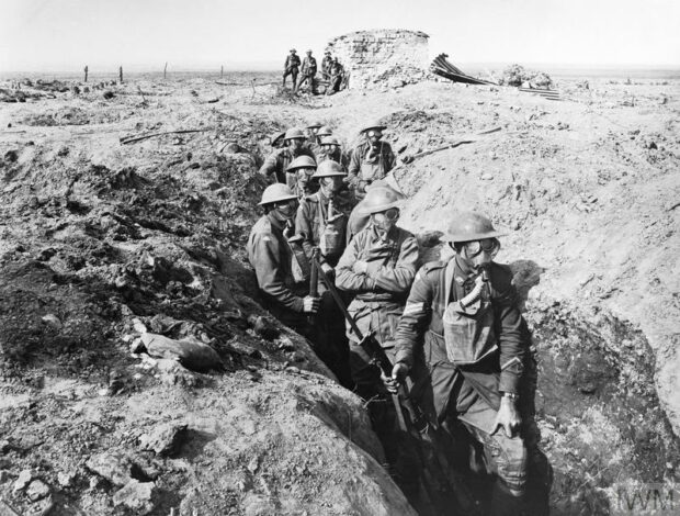 Soldiers wearing gas masks walk through trenches during World War One.